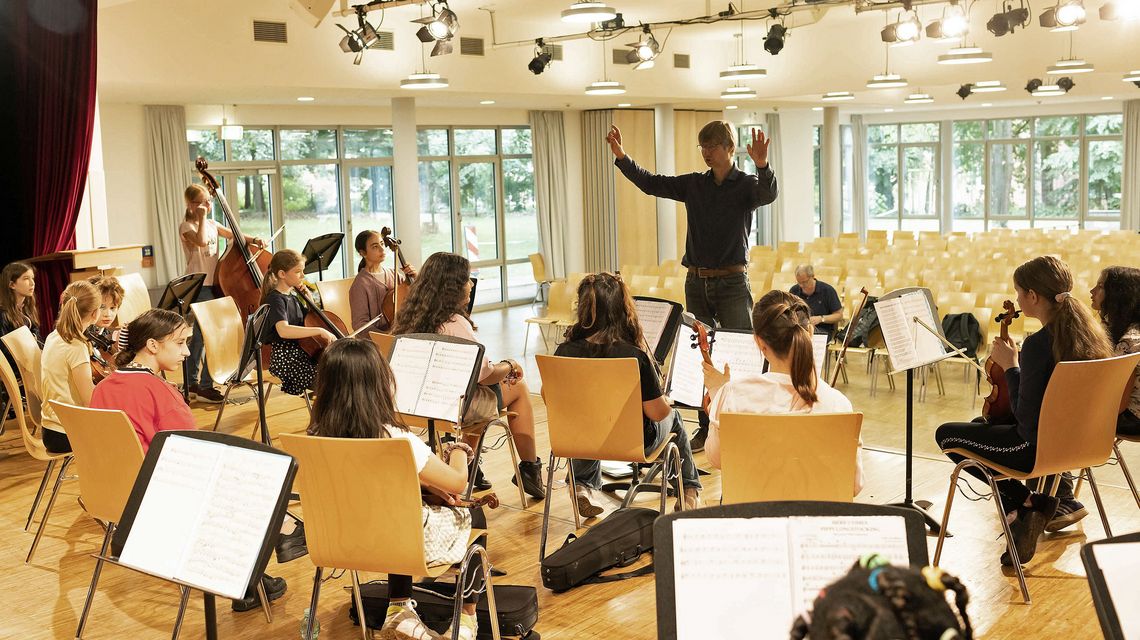 Wichern con Brio: Die Schülerinnen und Schüler sitzen mit ihren Musikinstrumenten auf der Bühne und achten auf die Zeichen des Dirigenten.