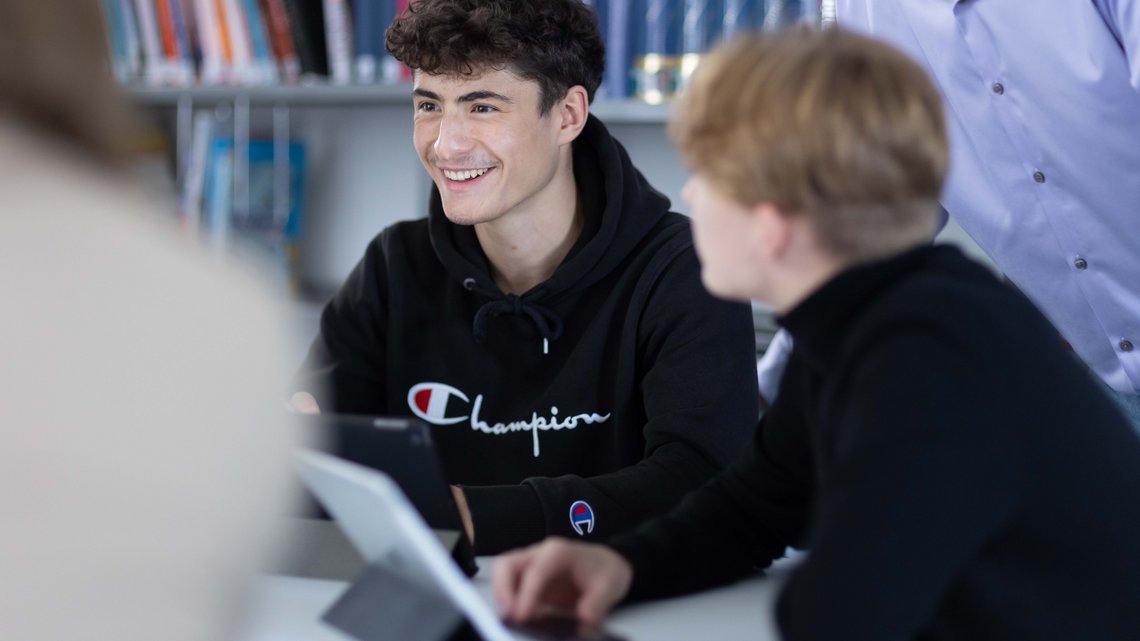 Zwei Schüler in der Bibliothek arbeiten in einer Gruppe mit ihren Tablets.