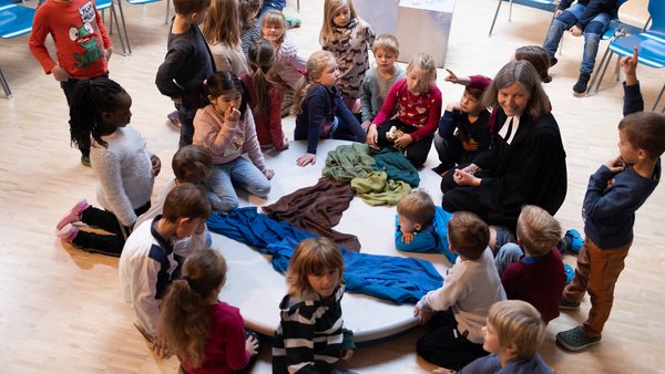 Andacht in der Grundschule: eine Gruppe von Kinder sitzt um eine gestaltete Mitte zusammen mit der Schulpastorin