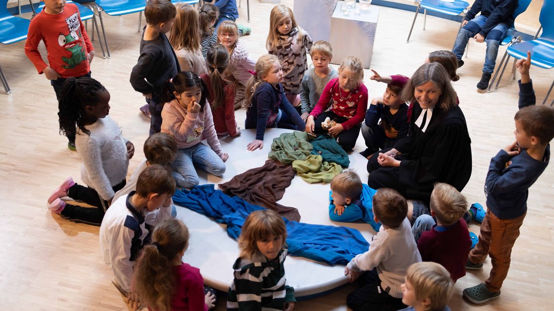 Andacht in der Grundschule: eine Gruppe von Kinder sitzt um eine gestaltete Mitte zusammen mit der Schulpastorin