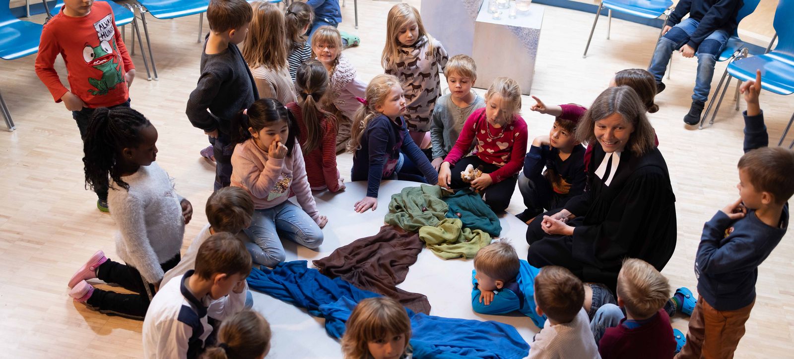 Andacht in der Grundschule: eine Gruppe von Kinder sitzt um eine gestaltete Mitte zusammen mit der Schulpastorin